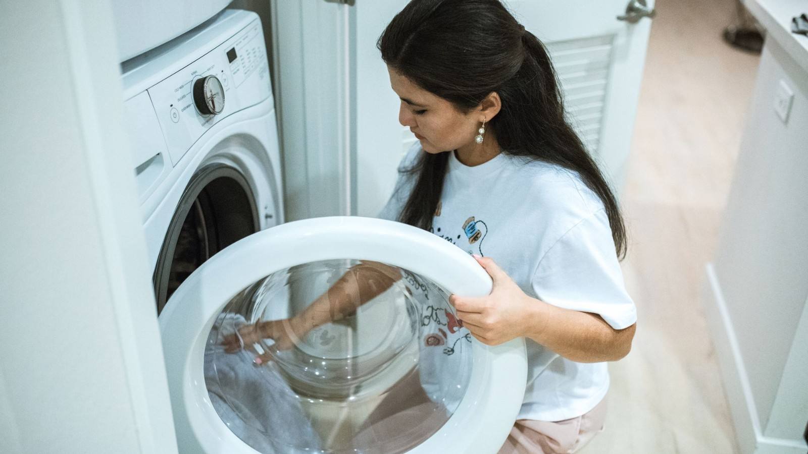 Person loading laundry into a white front-load washing machine